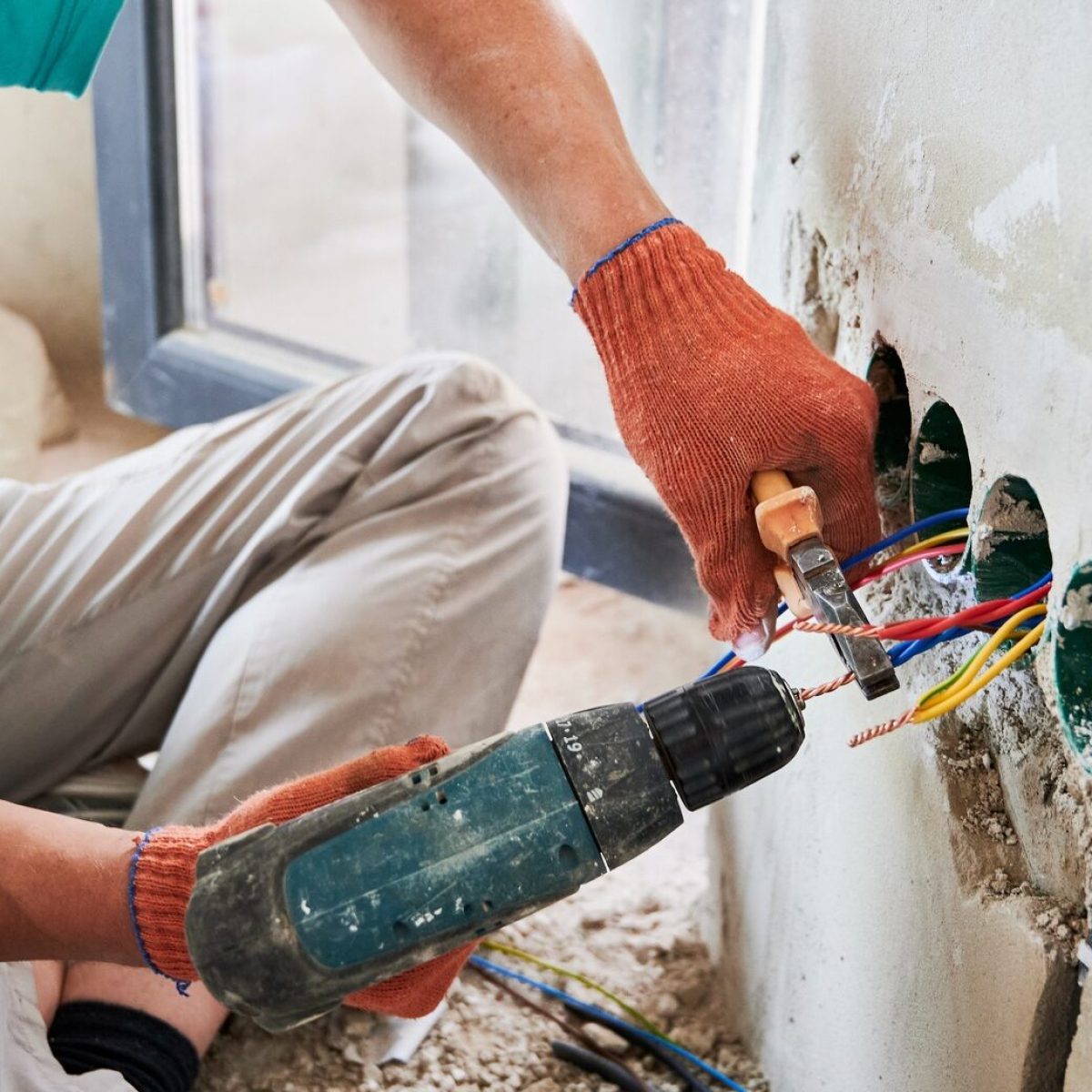 Male electrician using electric heat gun and pliers at home.